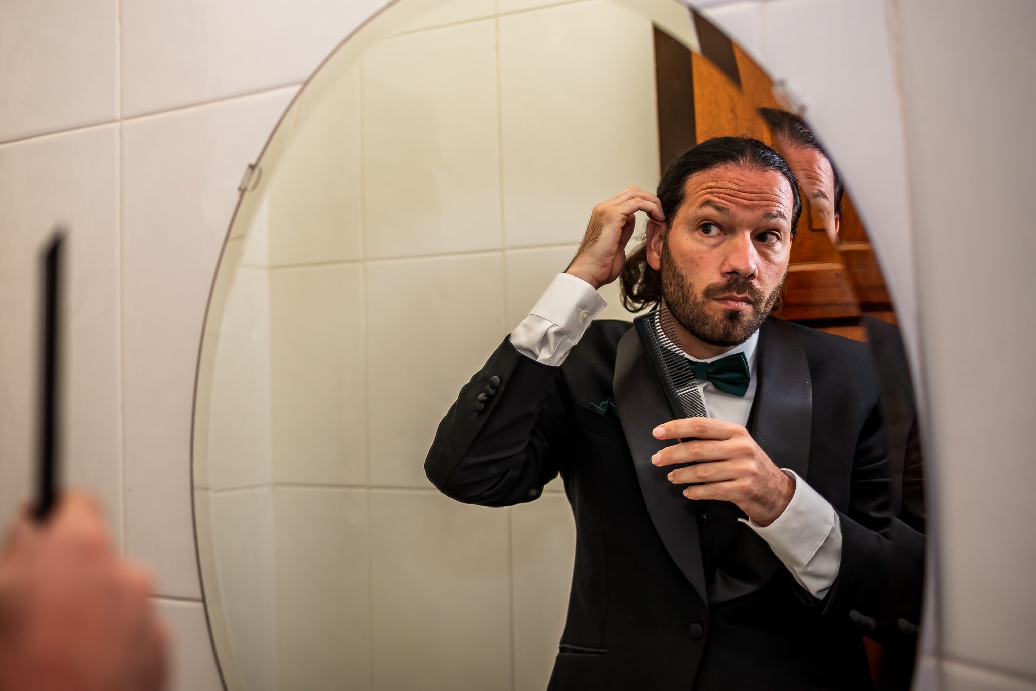 a groom gets ready for his wedding while looking in a mirror