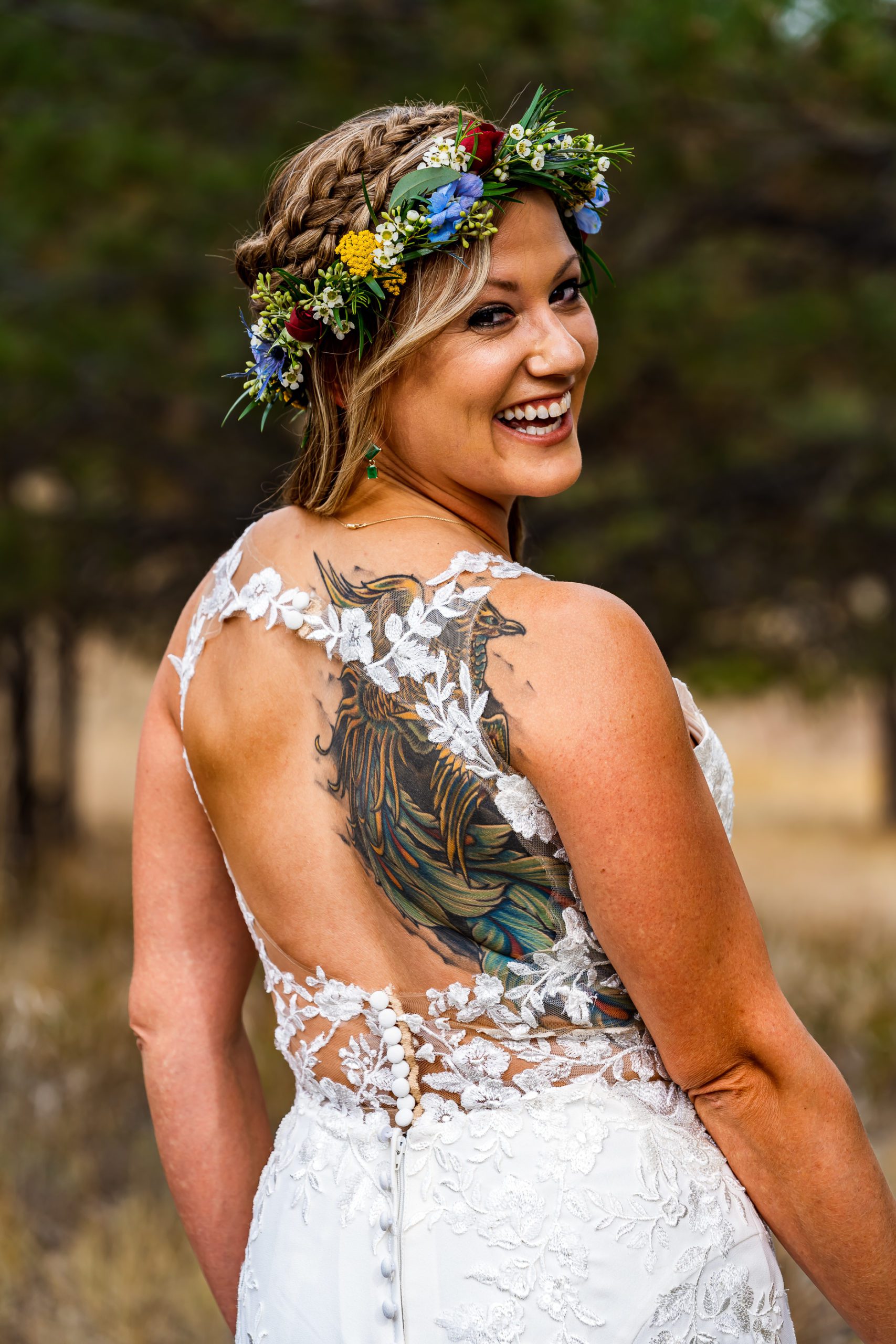 a tattooed bride wearing a flower crown showing out the lace cut out in the back of her white wedding dress.