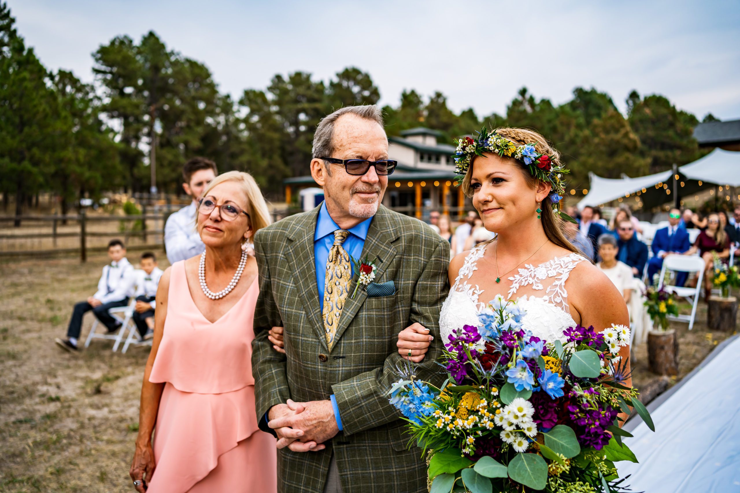 A bride is walked down the isle by her mother and father at a large backyard wedding in Colorado.