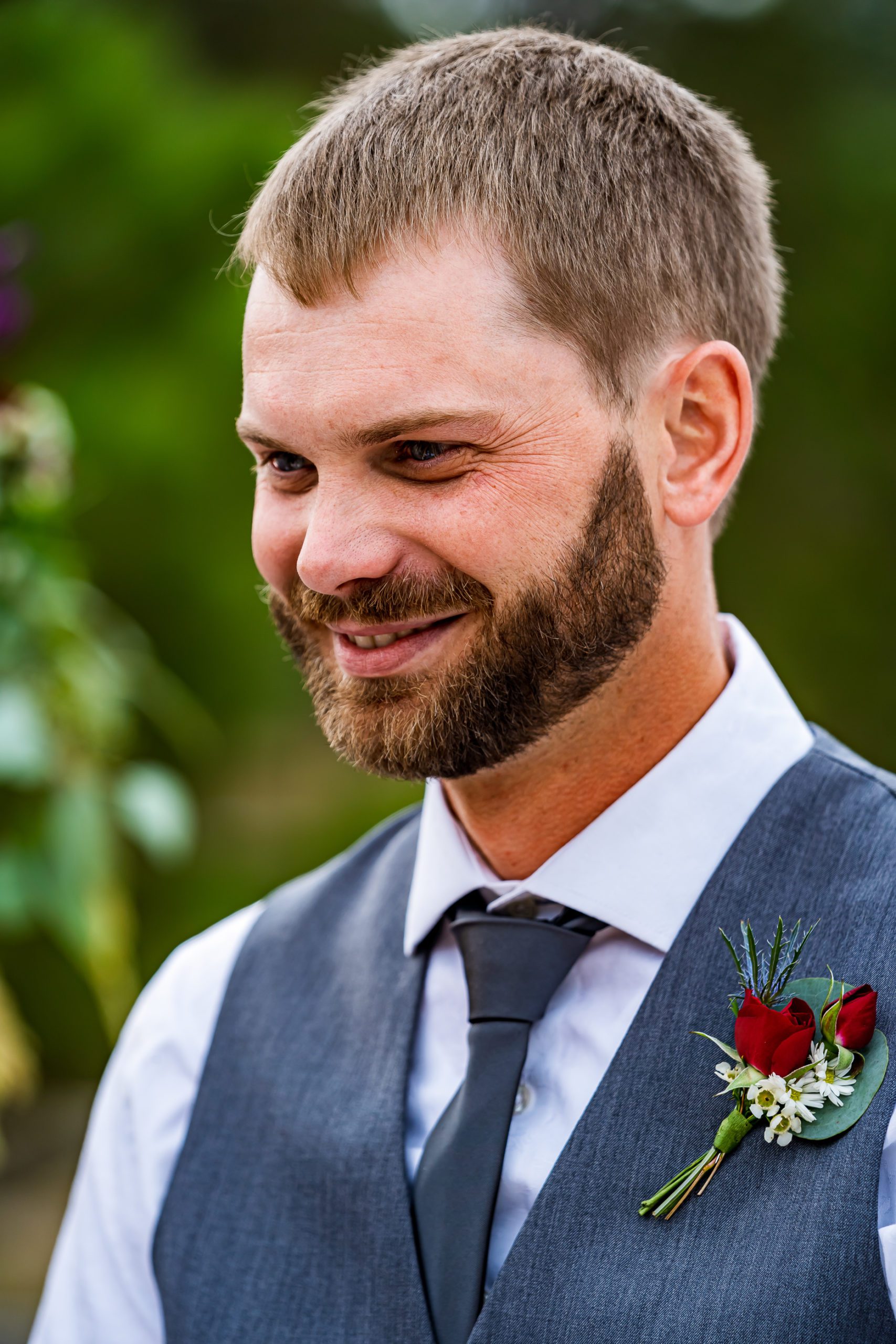 A groom with a grey vest and red roses in his boutonniere.