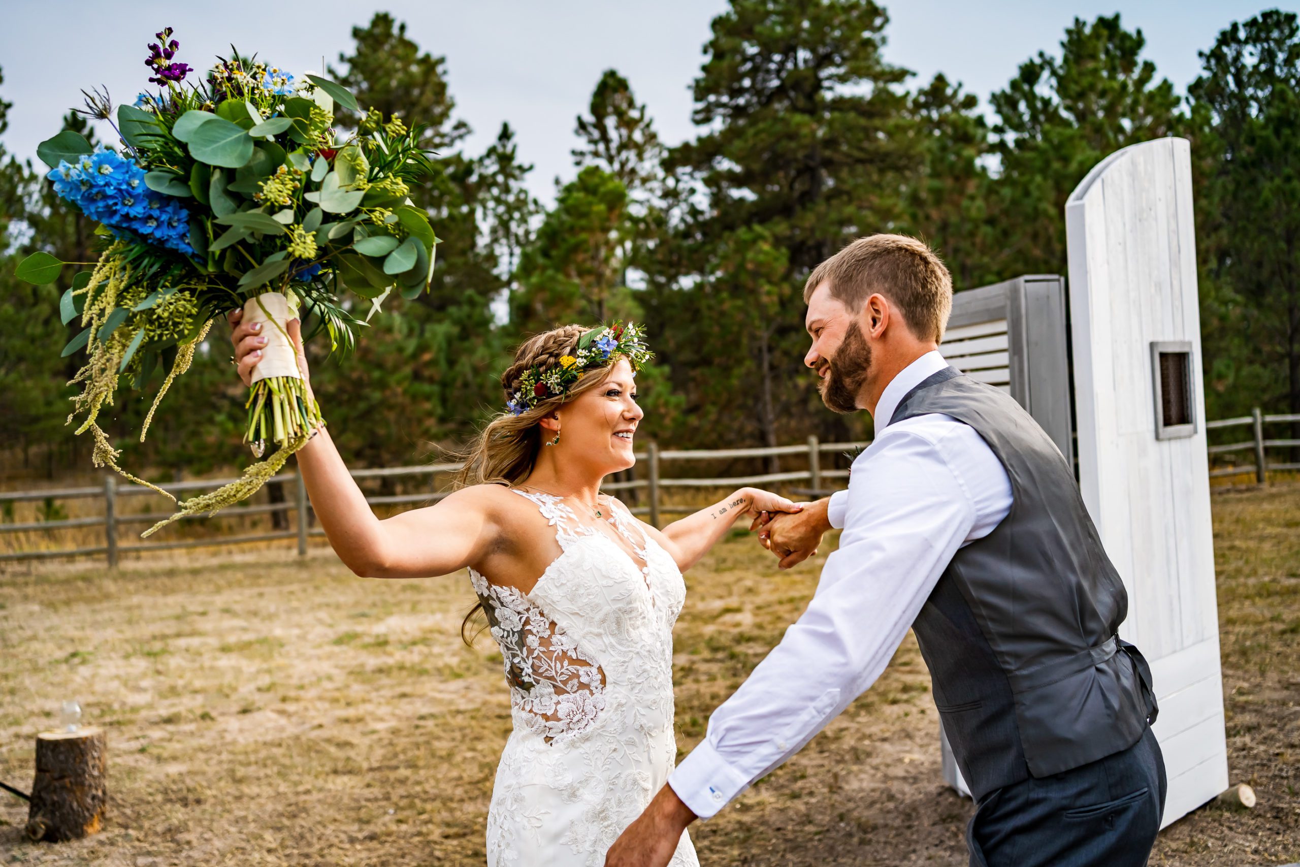 A bride in a white dress and flower crown opens up her arms with her bouquet in her hand to hug her groom after their backyard wedding in Colorado.
